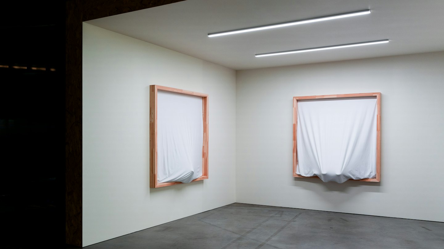 Two framed white fabric artworks mounted on a gallery wall.