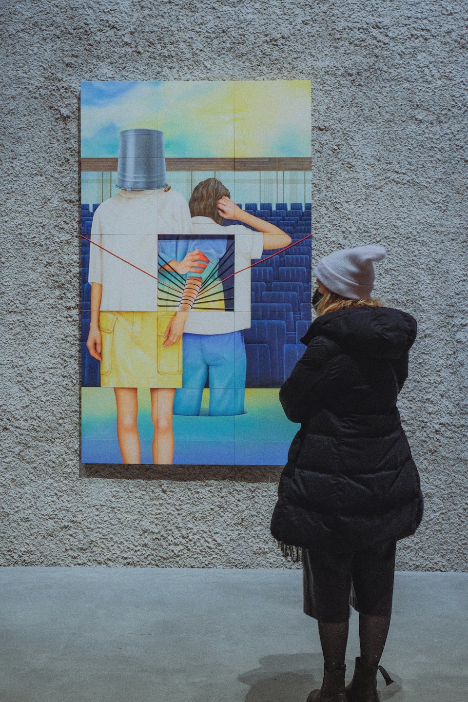Person in puffer jacket contemplates art in a gallery.