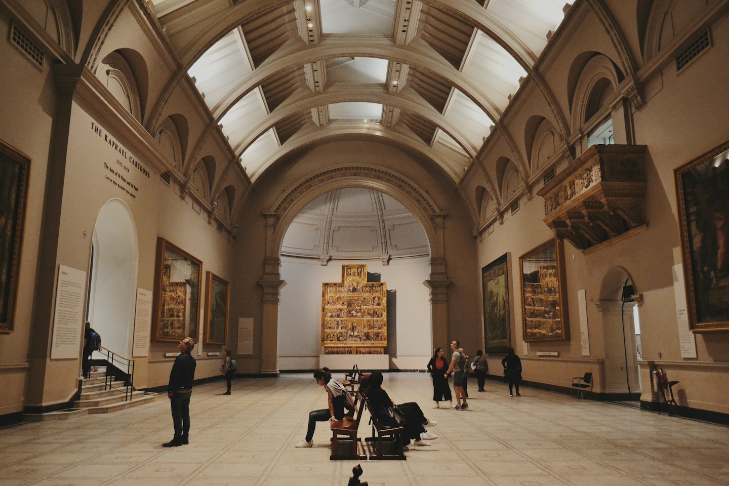 Museum visitors admire art under high vaulted ceilings.