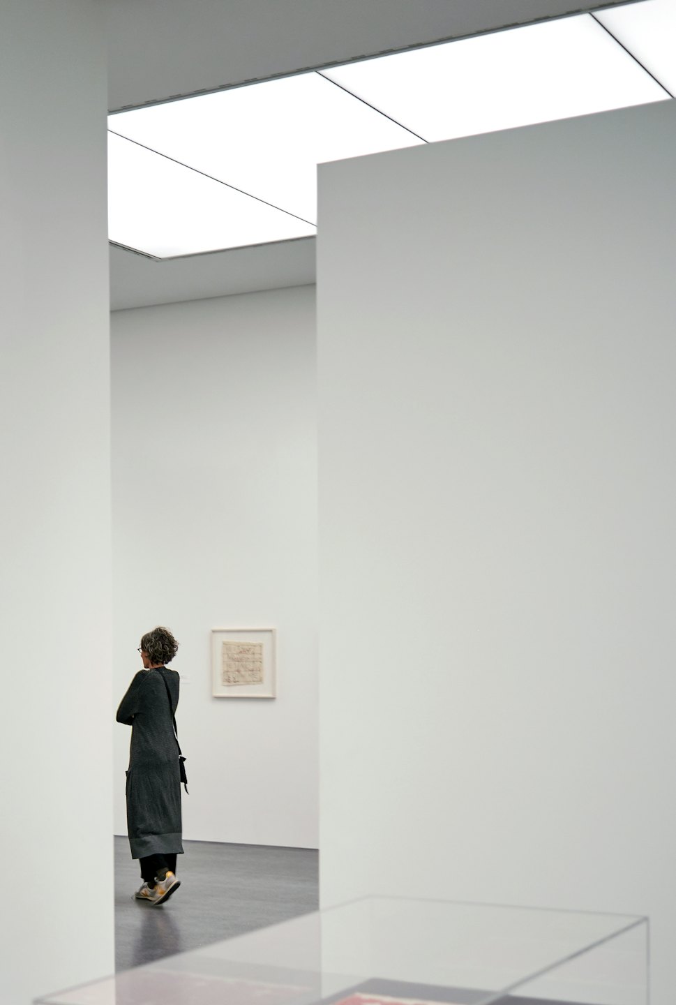 A visitor in a dark cardigan examines art in a gallery.